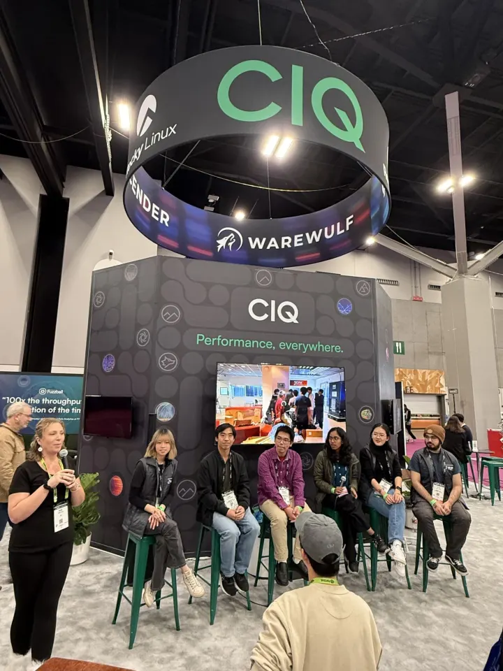A panel of students seated on stools under the CIQ booth ring while a host speaks