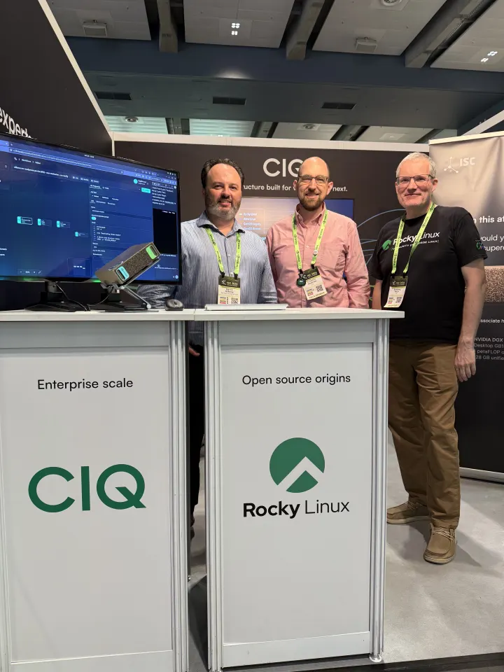 Three people behind CIQ and Rocky Linux booth counters next to a monitor running a Fuzzball workflow
