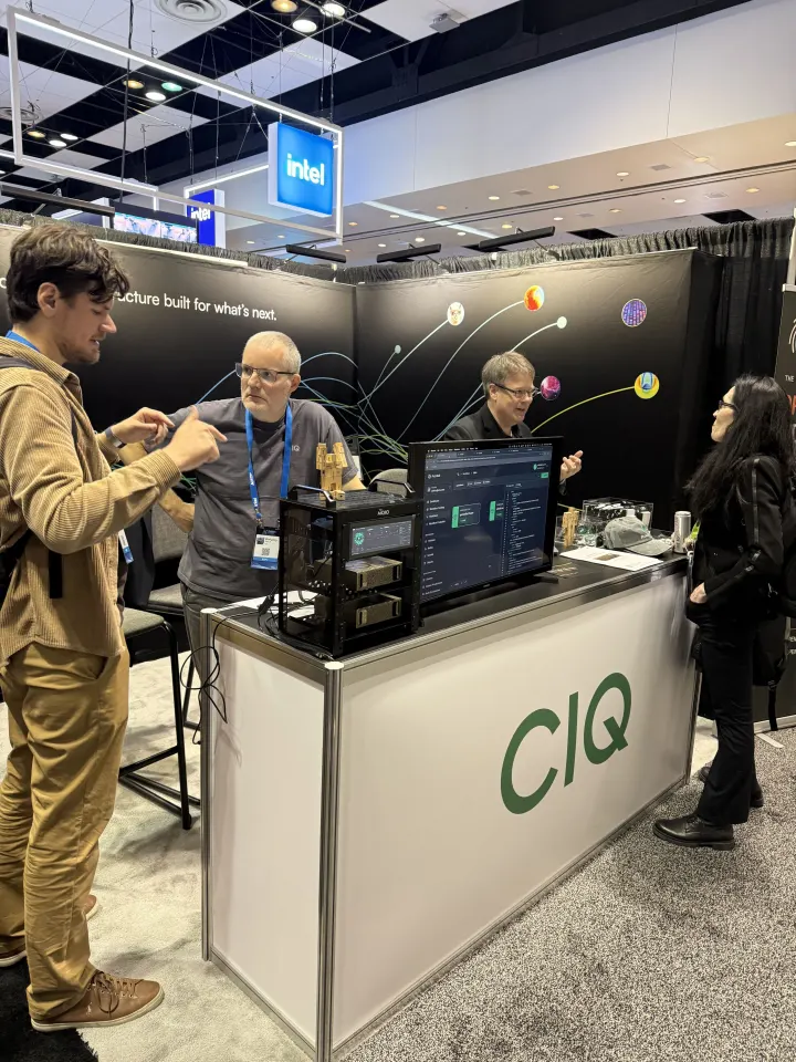 CIQ engineers talking with visitors at a booth counter with a Fuzzball workflow on screen